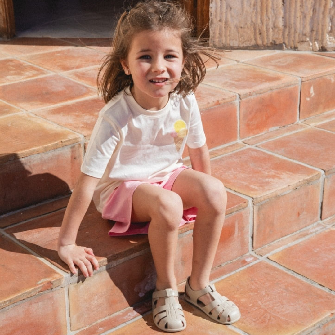 Menina sentada em escadas de azulejos terracota com t-shirt, saia e sandálias.