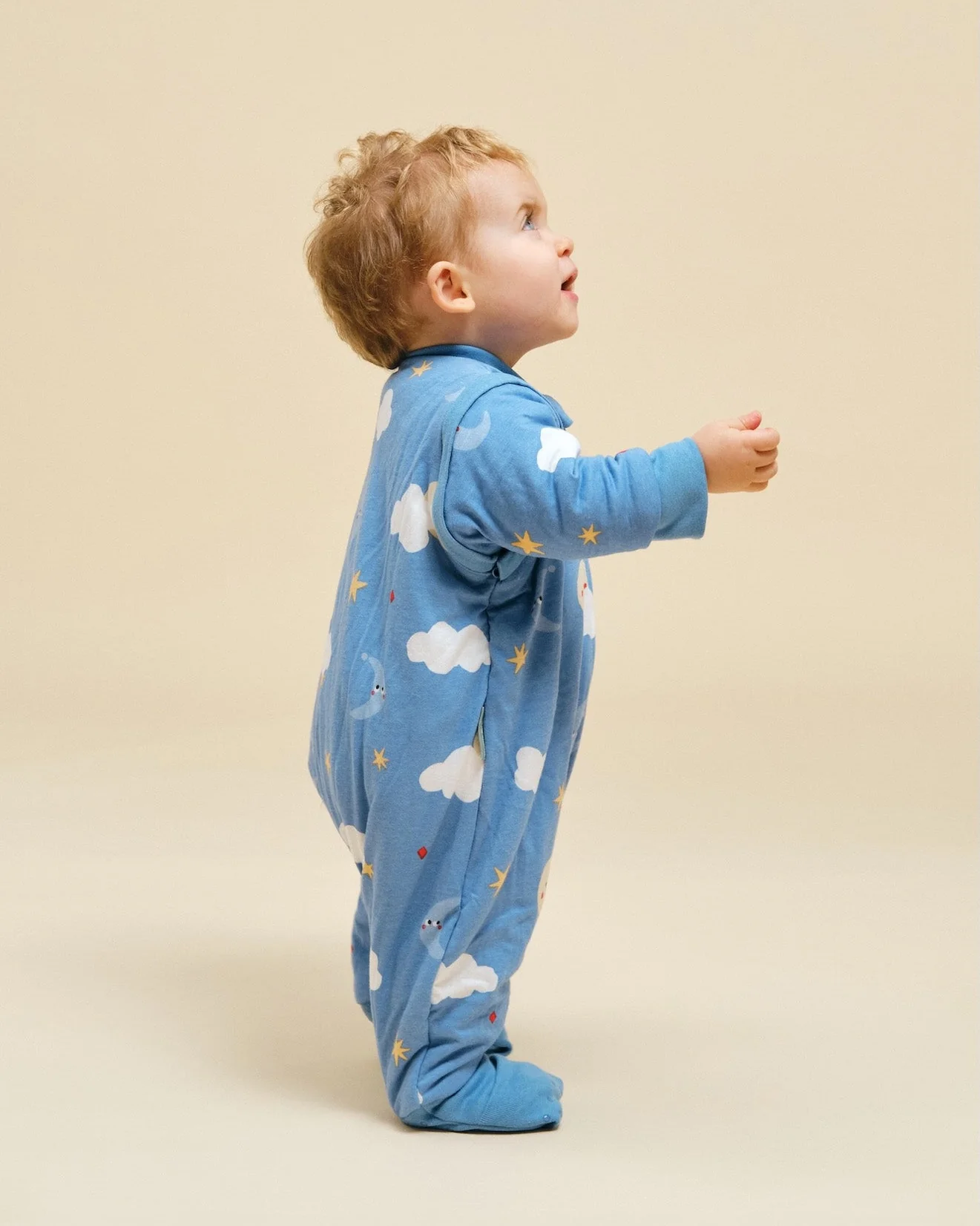 Criança de lado com macacão azul com estampado de nuvens e estrelas