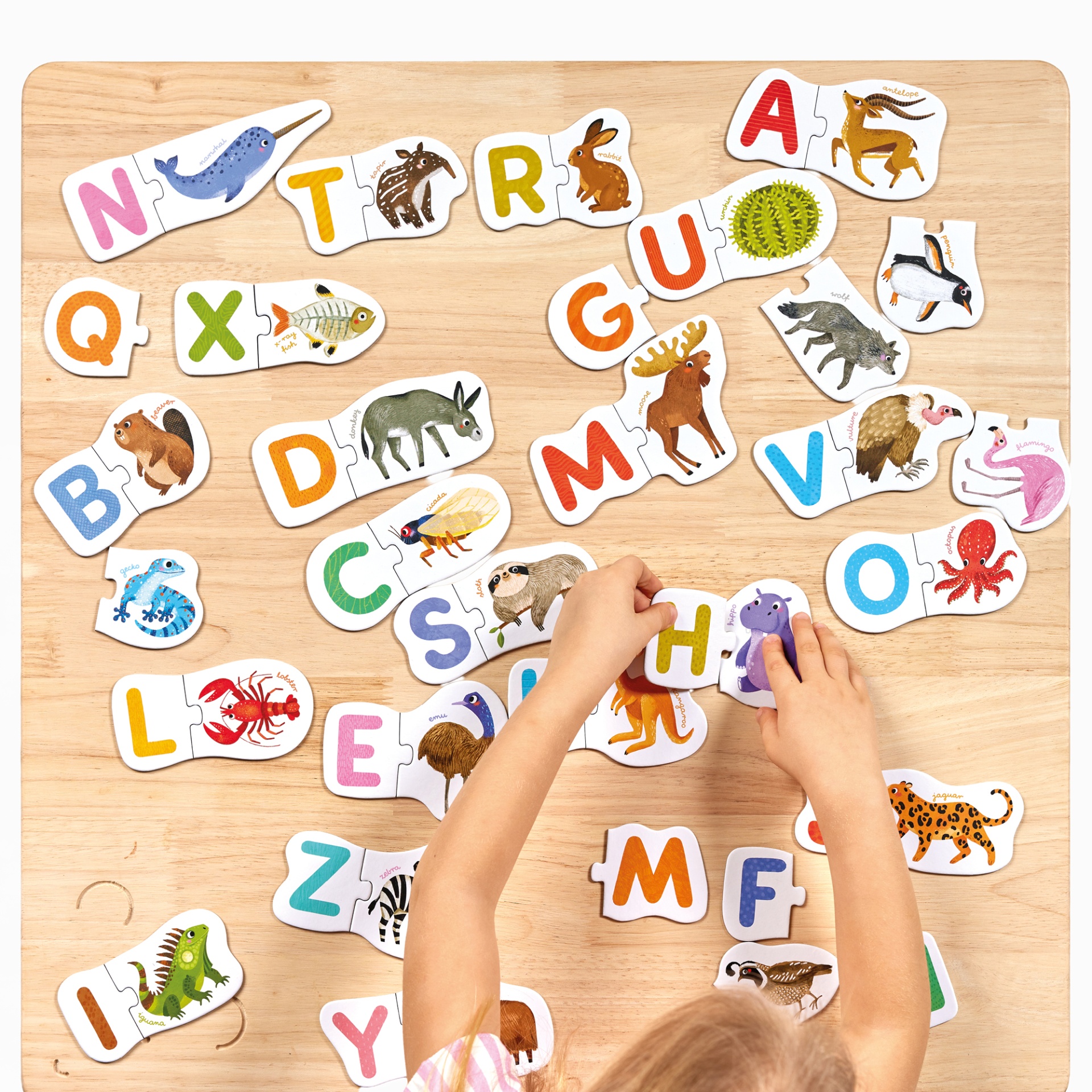 Puzzle infantil de letras e animais em cartão com mãos de criança montando sobre mesa de madeira.