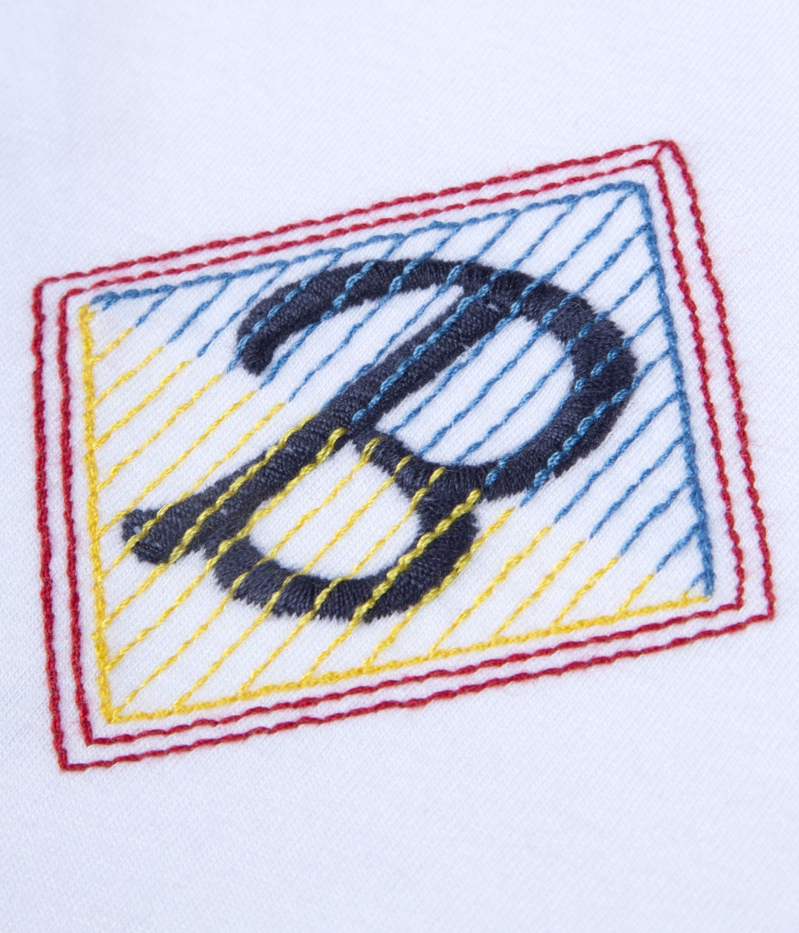 Bordado colorido em tecido branco com a letra D e linhas em vários padrões.