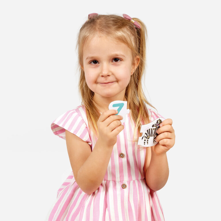 Menina de vestido rosa e branco segurando peças de puzzle com número 7 e zebra