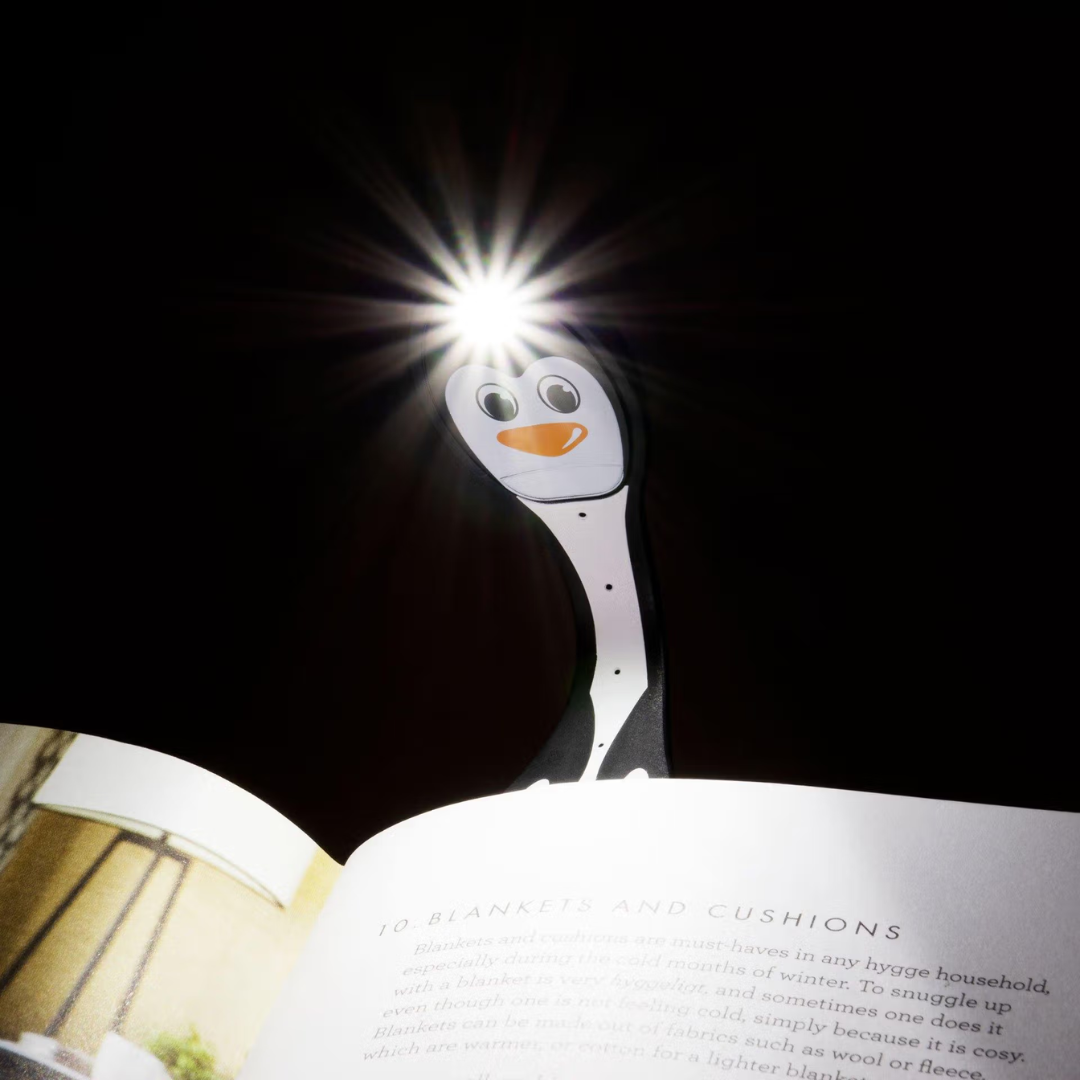 Luz de leitura em forma de pinguim a iluminar um livro aberto