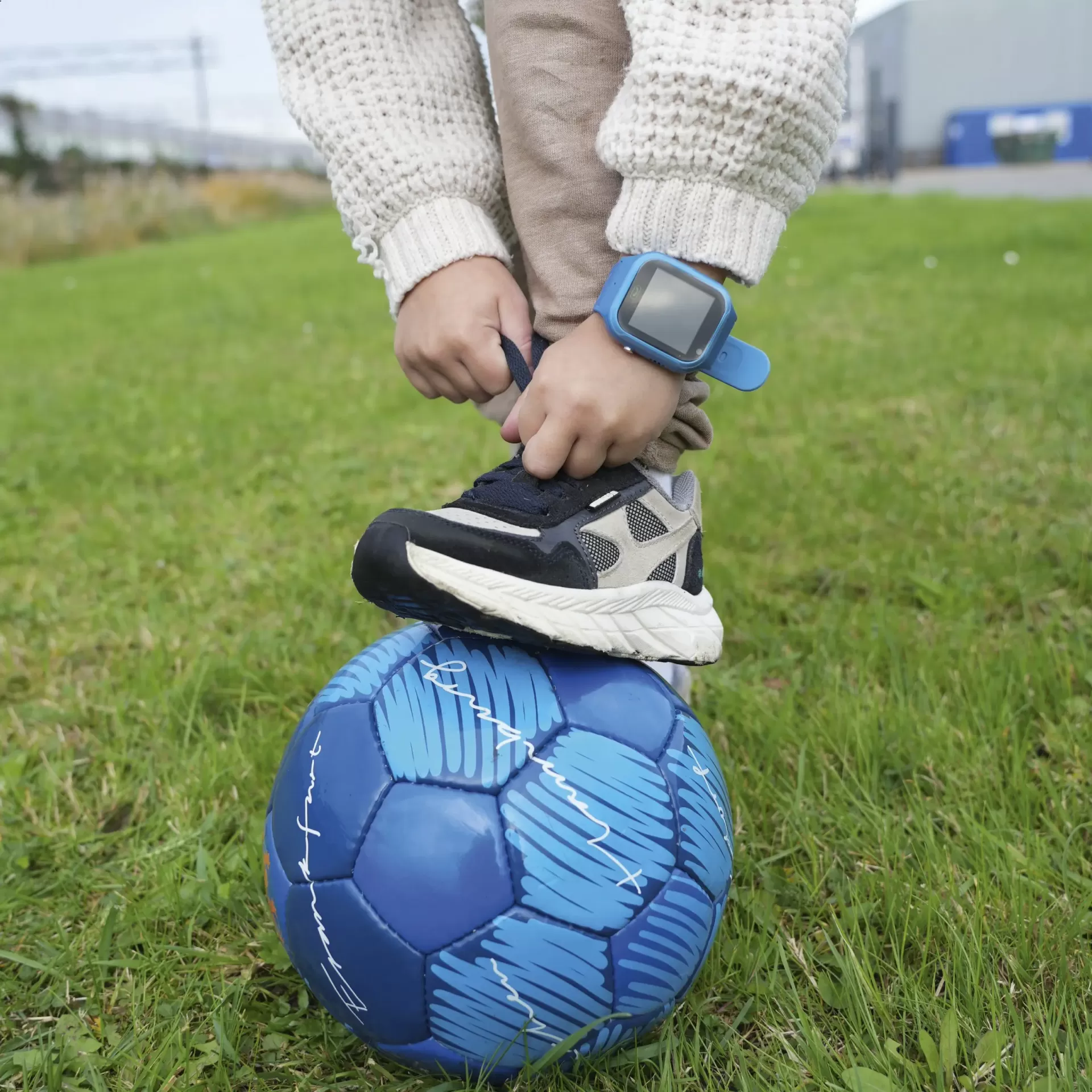 Criança com ténis a amarrar cadarço em bola de futebol azul no relvado