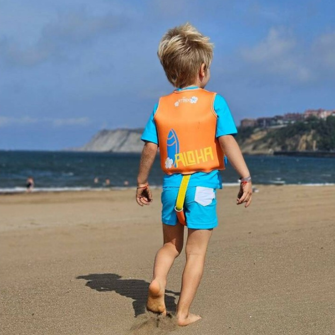 Criança na praia com colete salva-vidas laranja ALOHA e fato de banho azul claro
