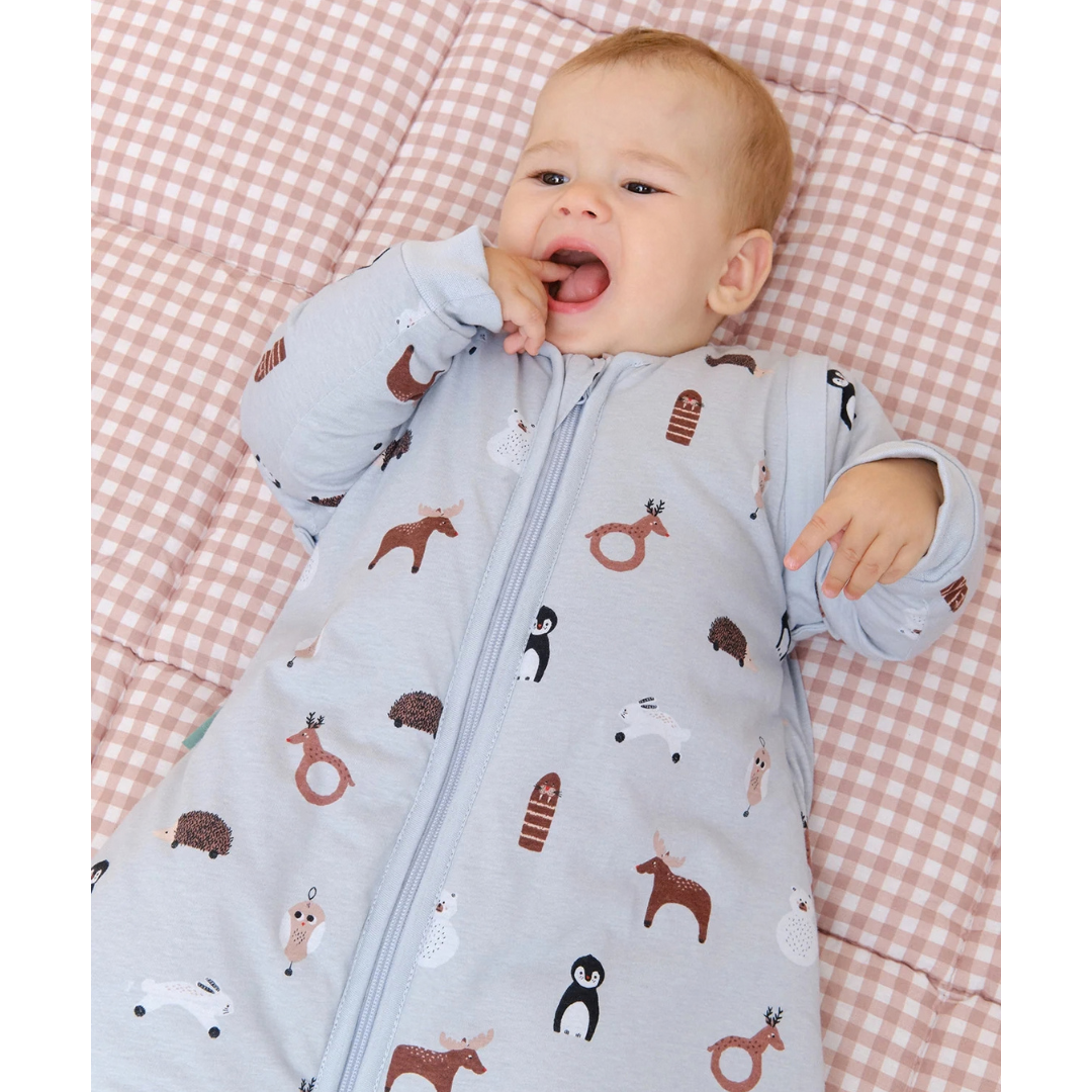 Bebé com saco de dormir cinzento estampado de animais a deitar num colchão xadrez bege e branco