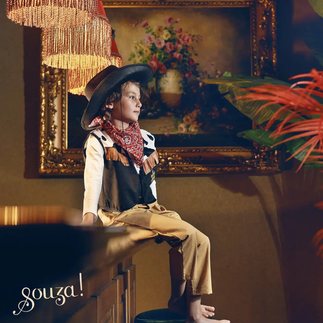 Criança vestindo roupa de cowboy sentada num móvel de madeira