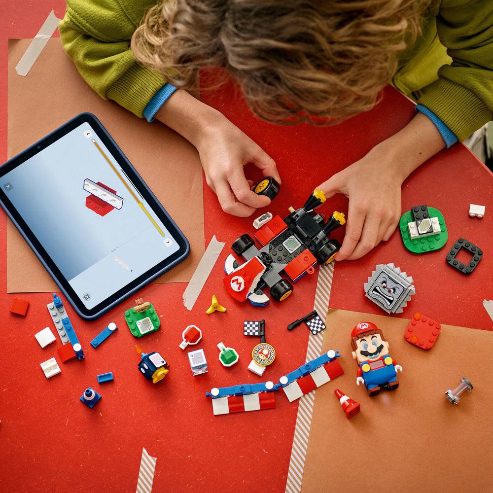 Criança a montar peças LEGO temáticas de Mario numa mesa com tablet