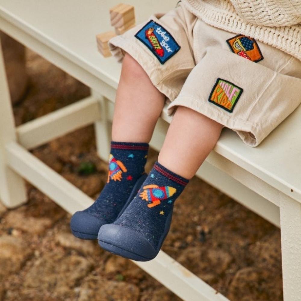 Meias azuis com padrão de foguete colorido e sola azul à criança sentada.