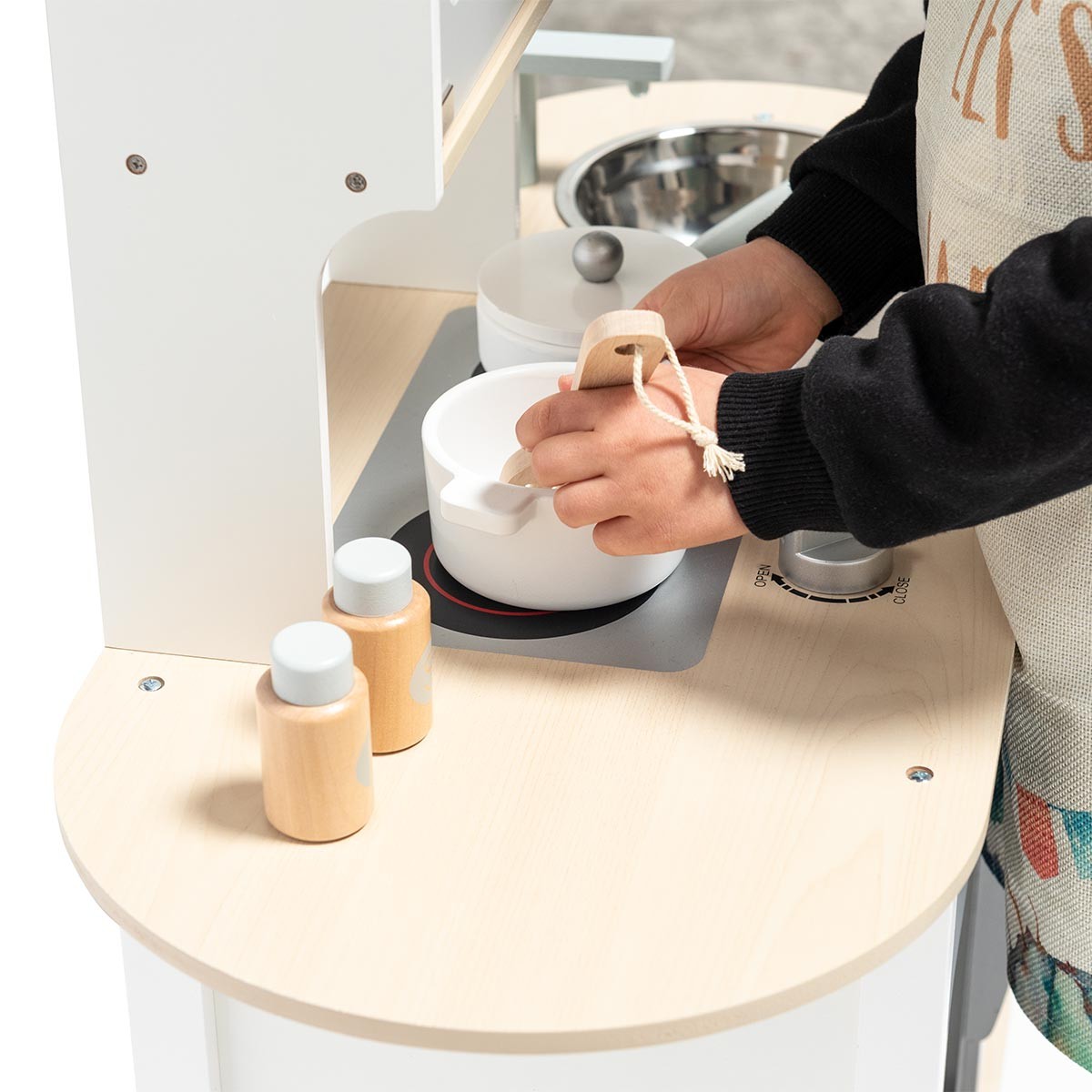 Criança a usar cozinha de brinquedo em madeira clara com frascos e tacho branco