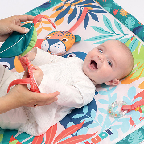 Bebé sorridente deitada em tapete de atividades colorido com brinquedos suspensos
