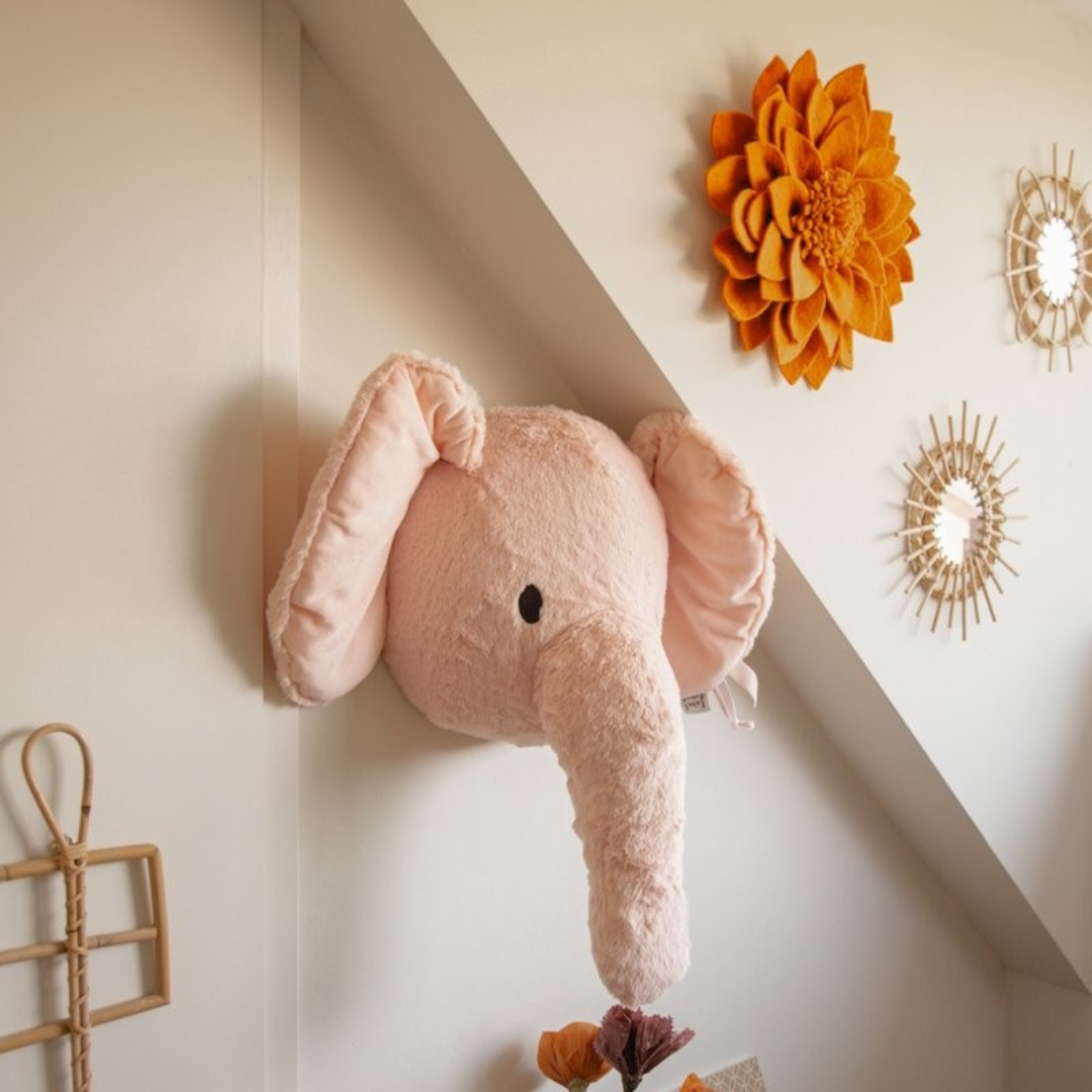 Cabeça de elefante de peluche rosa pendurada numa parede decorada com motivos solares de parede.