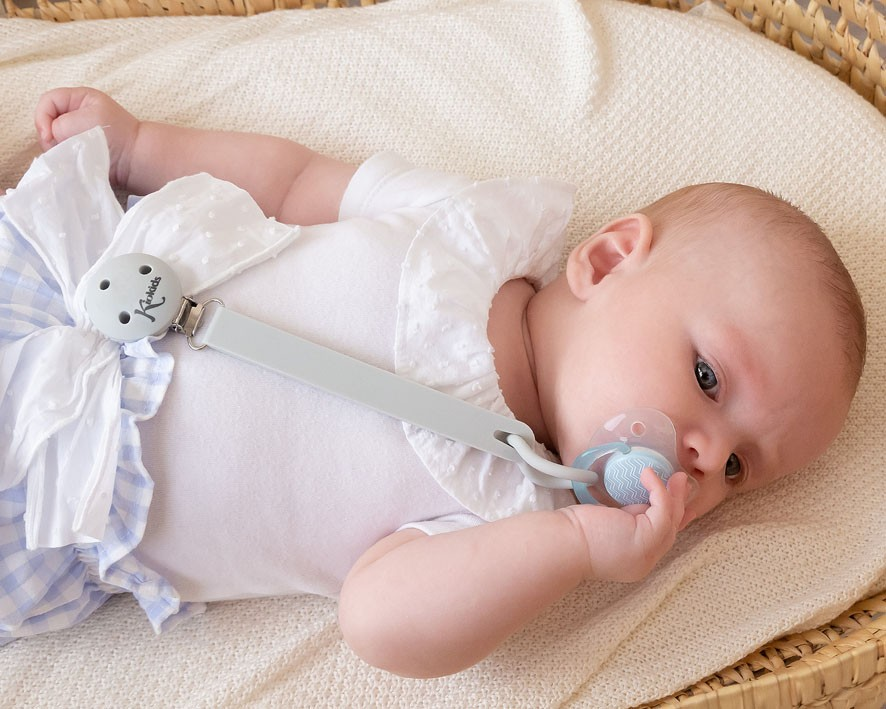 Bebé com chupeta presa a clip cinzento a descansar num berço de vime