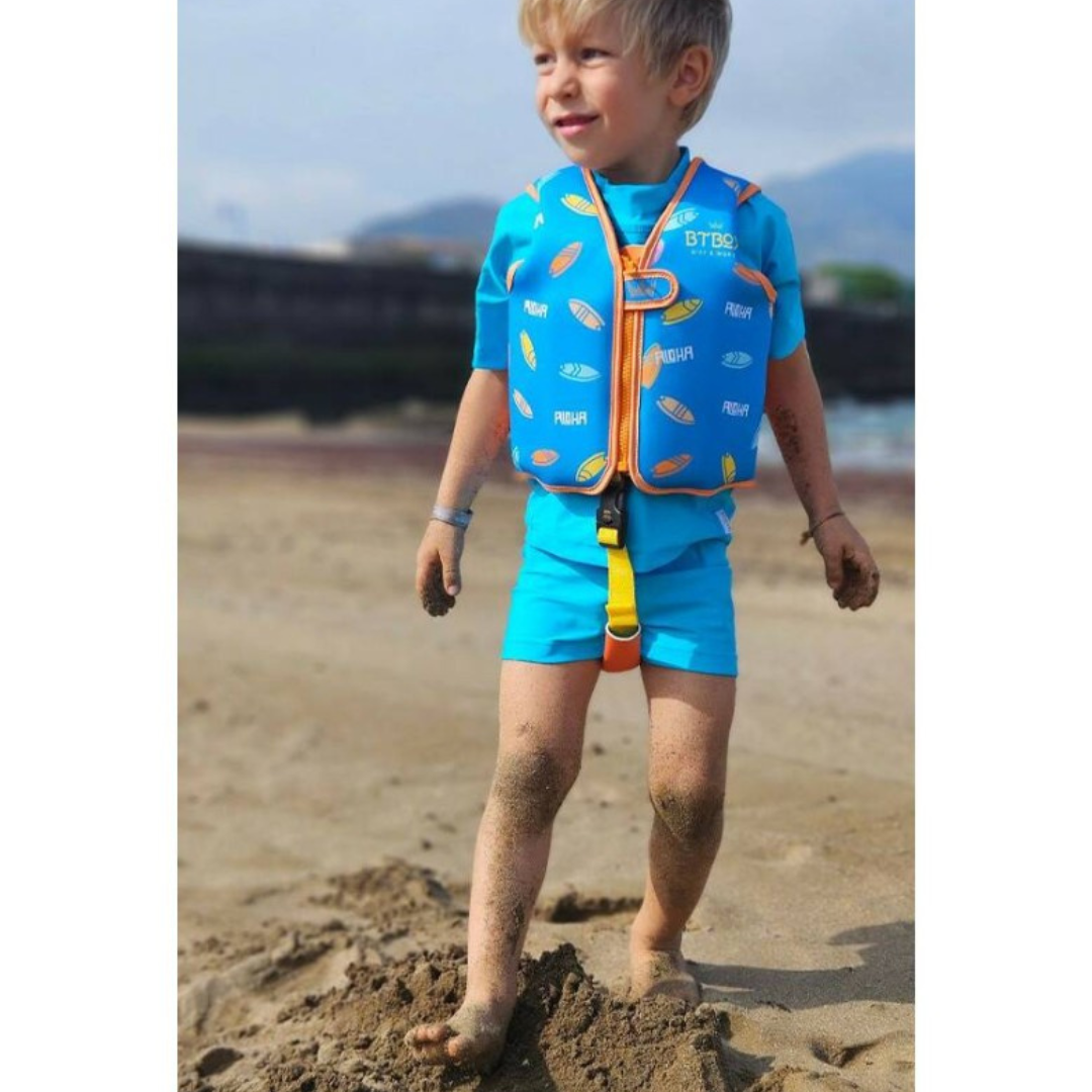 Criança na praia com colete salva-vidas azul e roupa azul