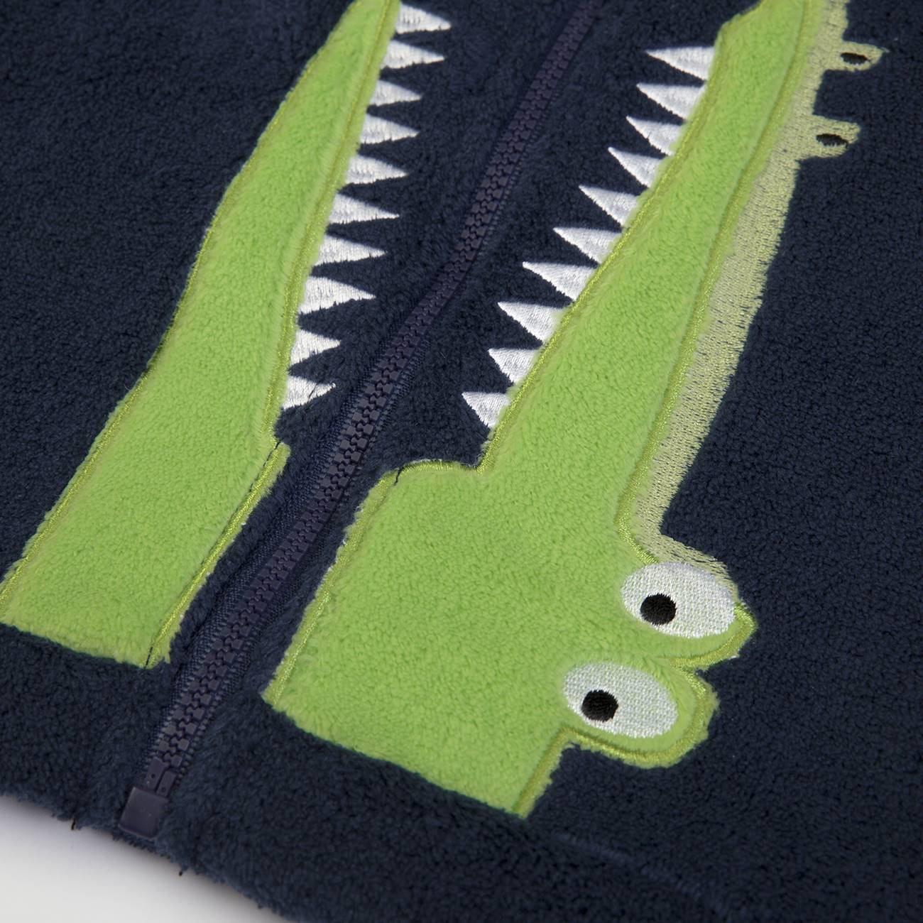 Casaco azul escuro com desenho de crocodilo verde e dentes brancos ao redor do fecho
