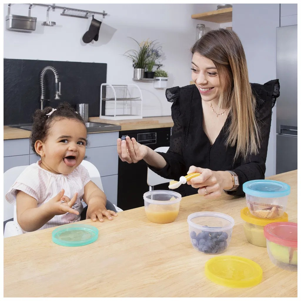 Recipientes de plástico com comida para criança numa cozinha com mulher e criança
