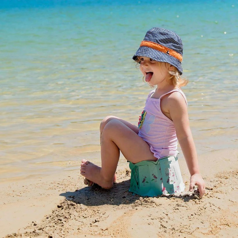 Criança sentada na praia com chapéu às riscas e fato de banho rosa