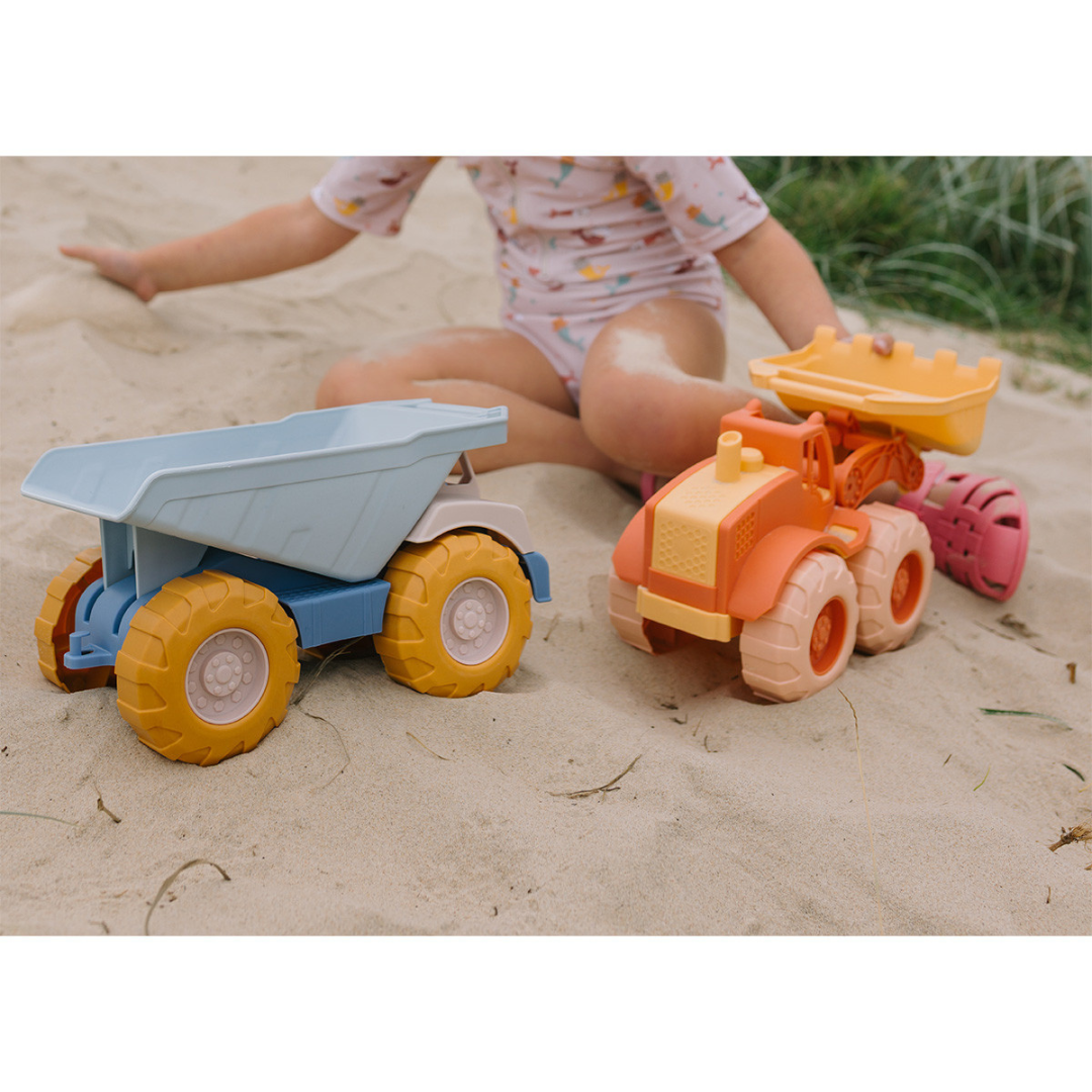 Carrinhas de brinquedo em plástico na areia com criança ao fundo