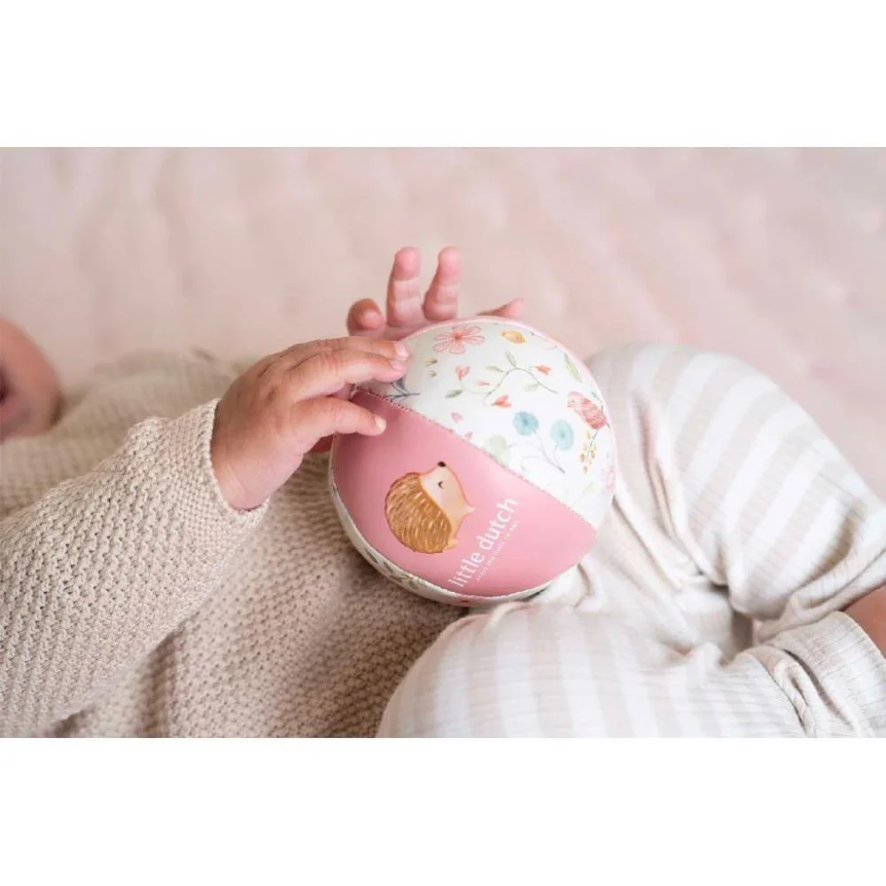 Bola de brincar colorida segurada por bebé com roupa creme tricotada e calças listradas