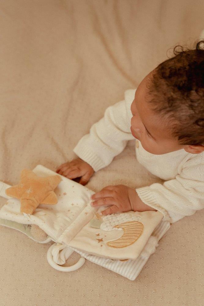 Bebé a brincar com livro de tecido macio em tons neutros