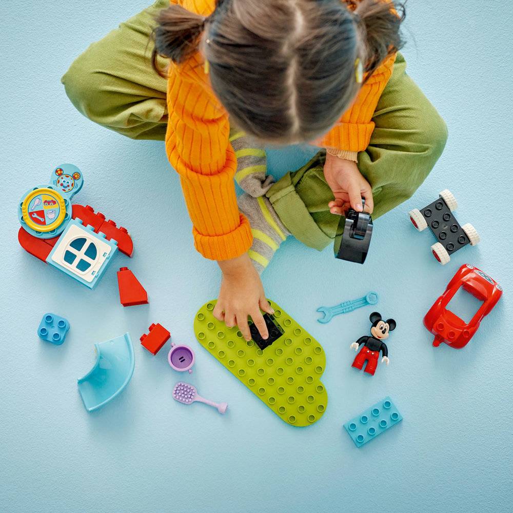 Criança a brincar com blocos de construção coloridos e figura do Mickey Mouse em tapete azul