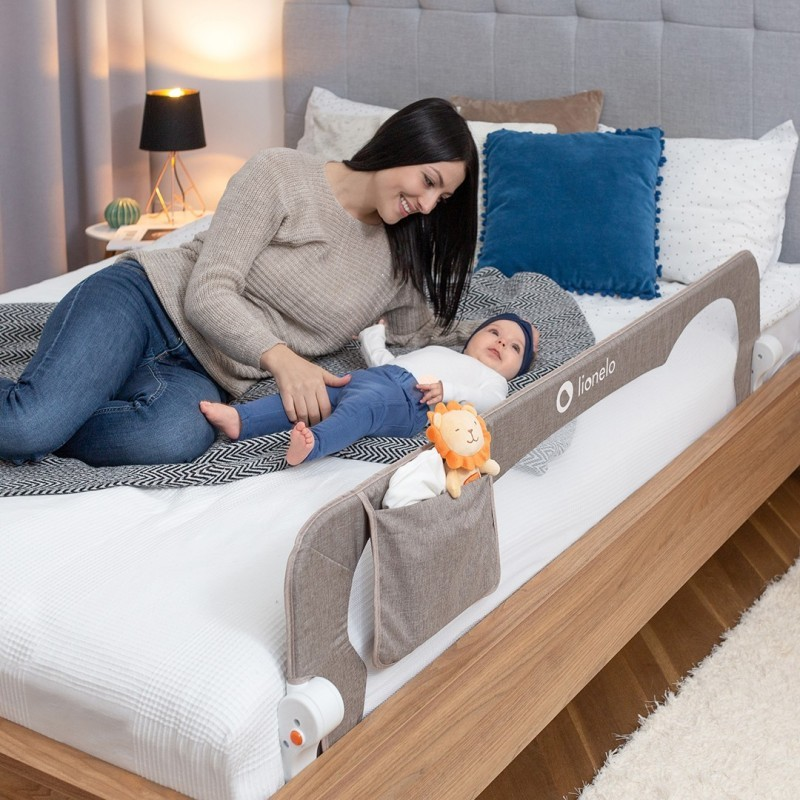 Cama com protetor de berço cinza e criança deitada com mulher ao lado