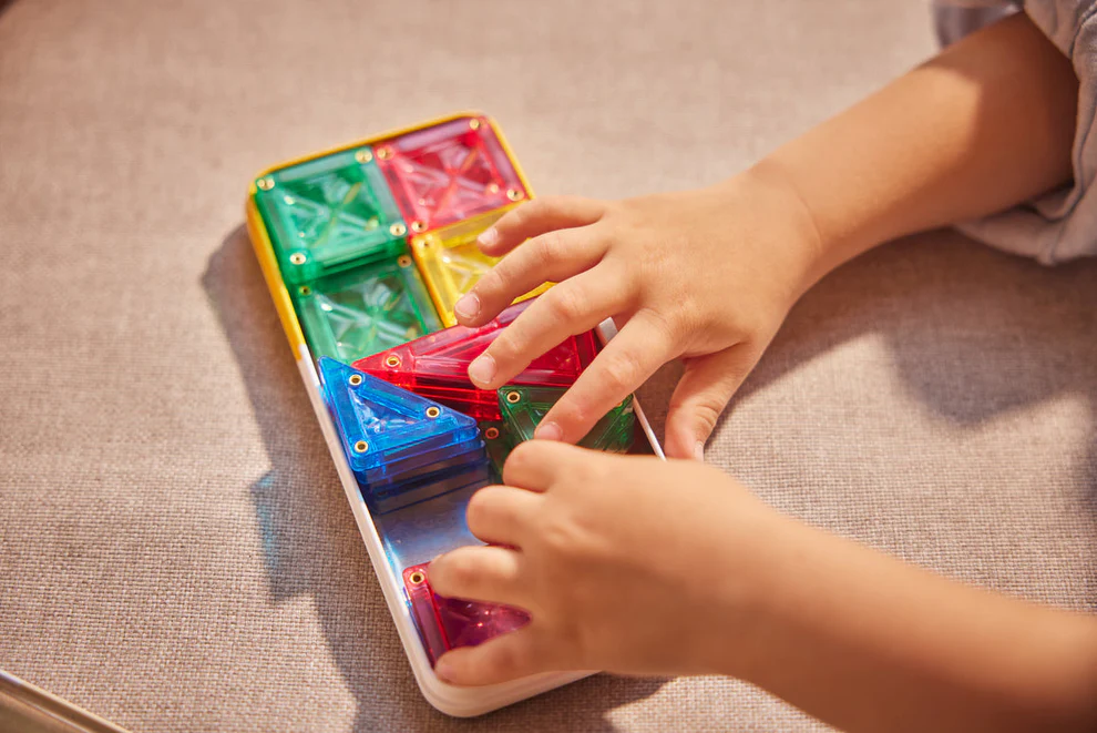 Mãos infantis com peças magnéticas coloridas num tabuleiro branco