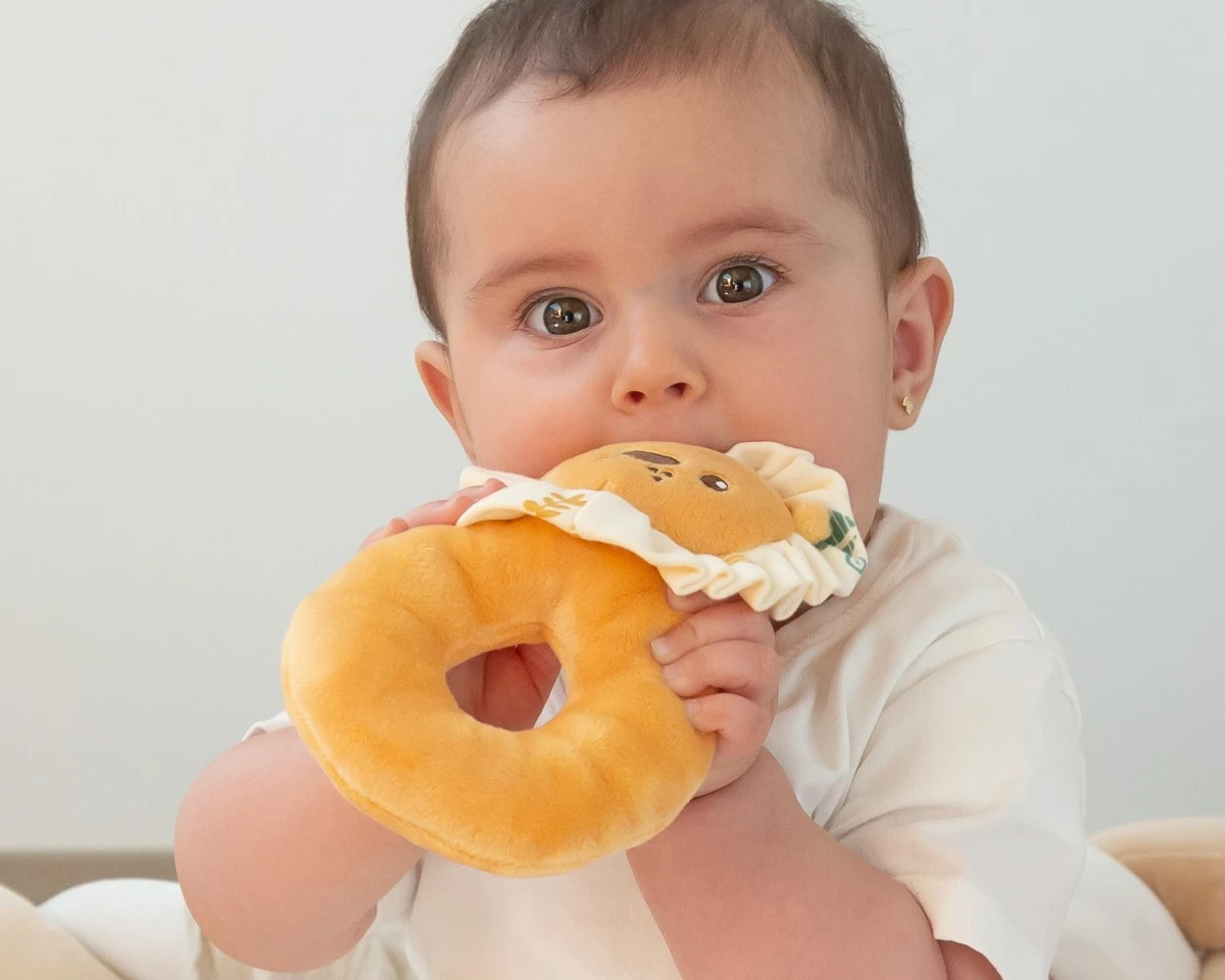 Bebé a morder brinquedo de peluche amarelo em forma de leão