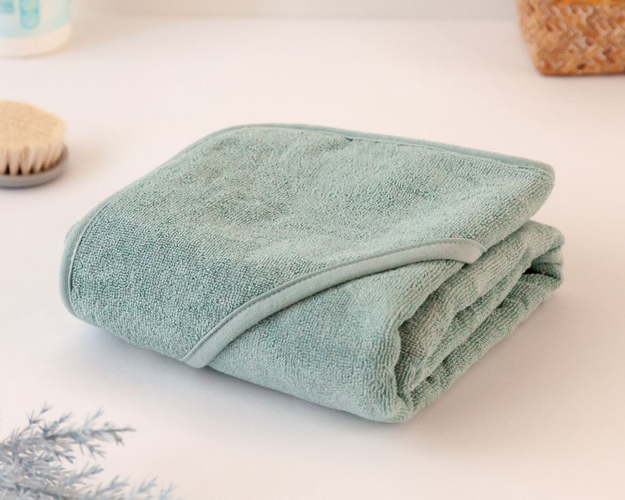 Toalha de banho azul esverdeado dobrada em superfície branca