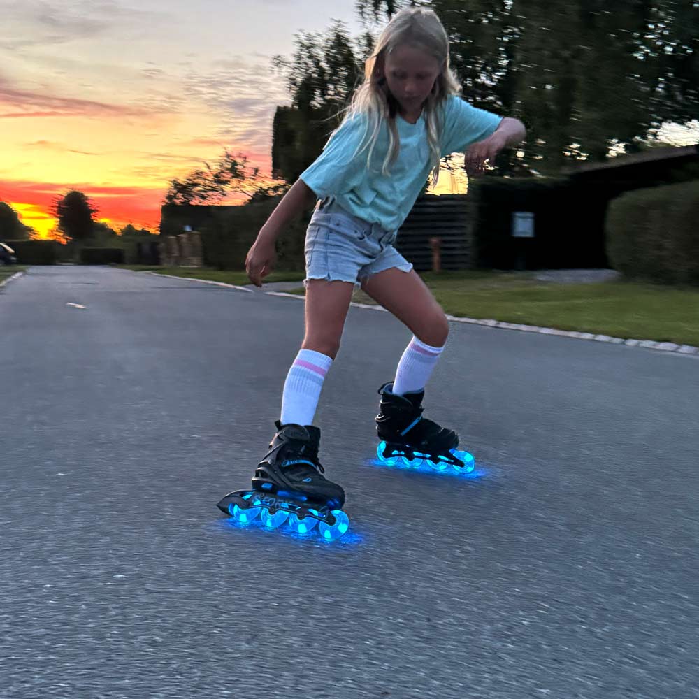 Criança a andar de patins em linha com rodas LED azuis numa rua ao pôr do sol