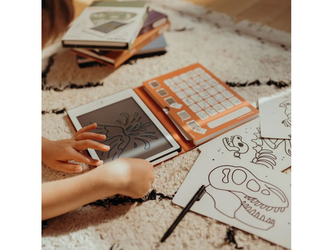 Criança a desenhar num tablet com capa laranja e desenhos de dinossauros no chão