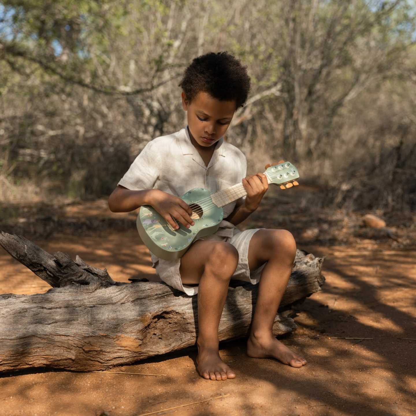 Criança com ukulele verde numa floresta seca