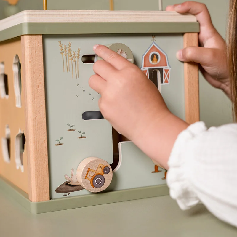 Brinquedo de madeira com ilustrações de quinta e rodas móveis, criança a mexer no brinquedo numa mesa verde claro.