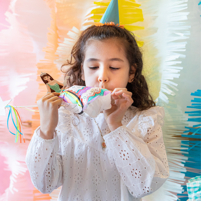 Criança com chifre insuflável de unicórnio colorido e roupa branca num ambiente decorado para festa