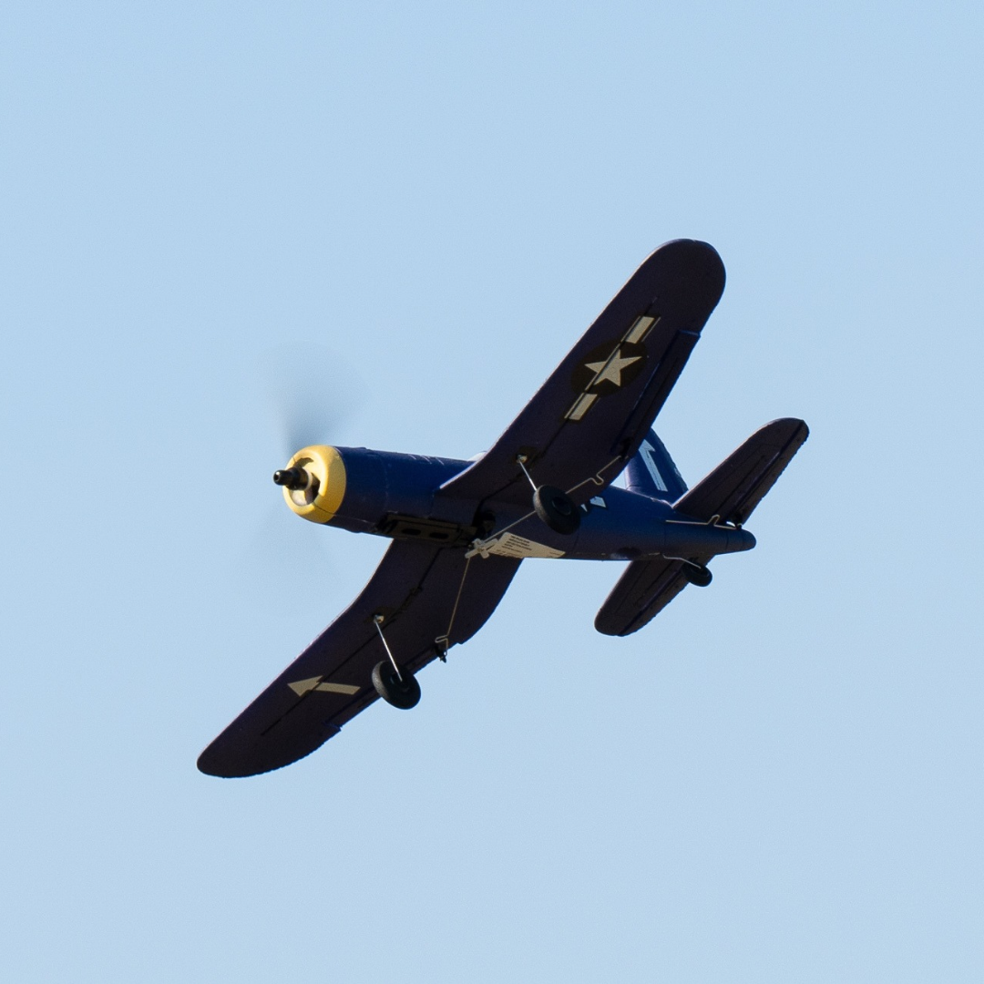 avião modelo de aeromodelismo azul escuro com detalhes amarelos em voo