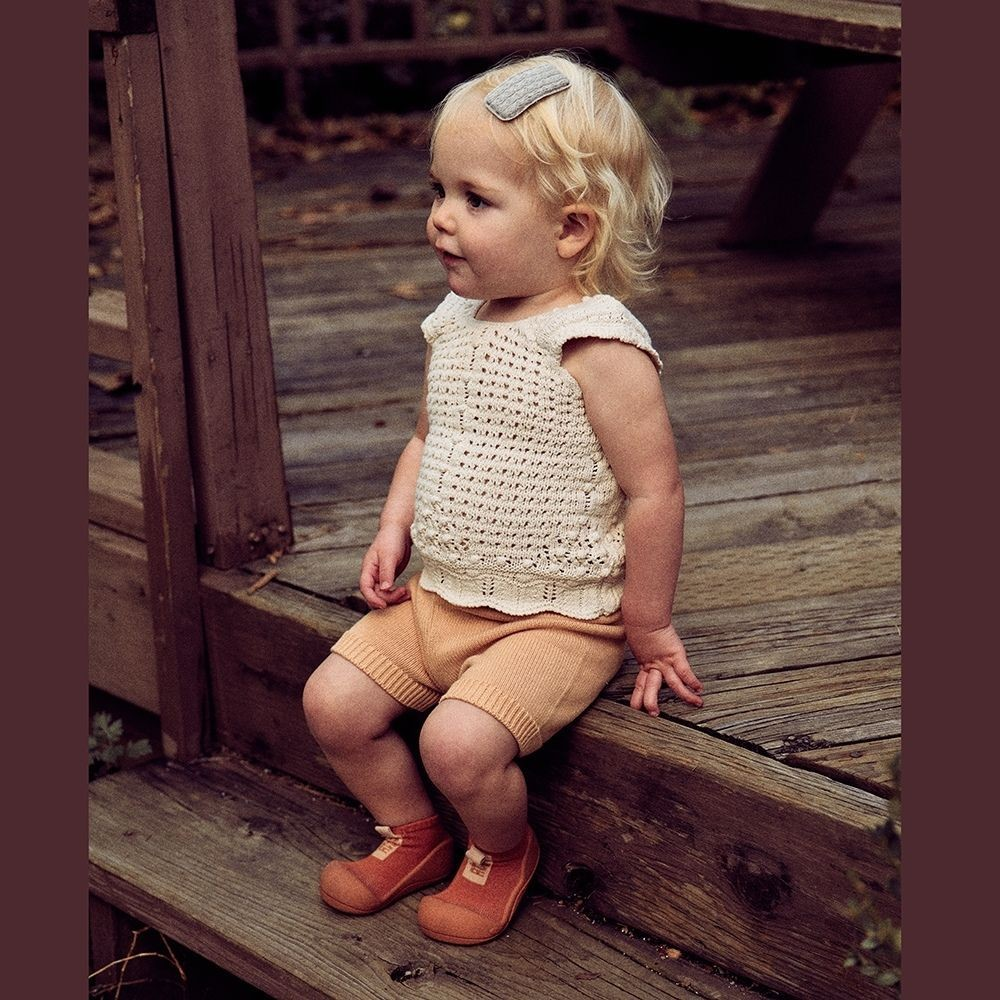 Criança com roupa de malha sentada em degrau de madeira exterior