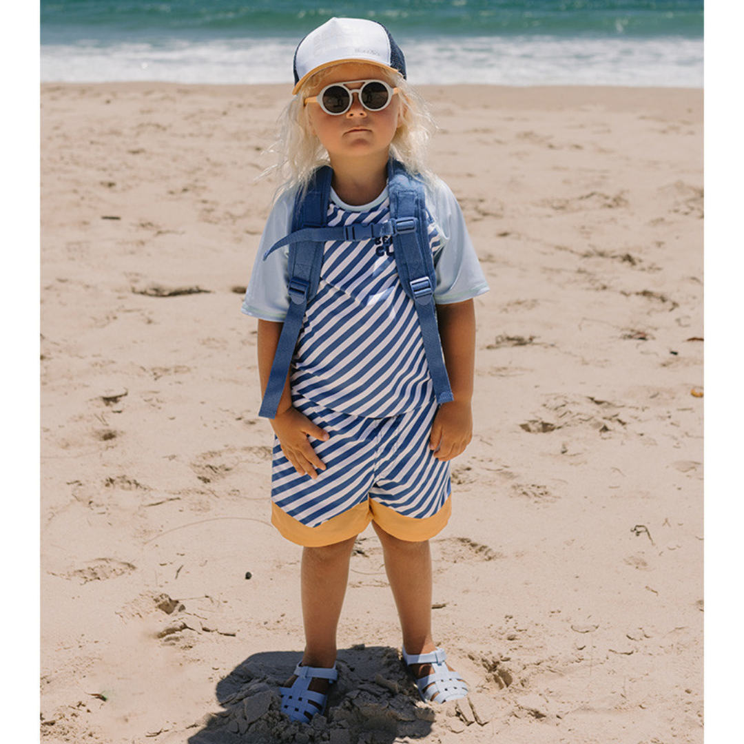 Criança com fato de banho riscado azul e branco com sandálias e mochila azuis na praia