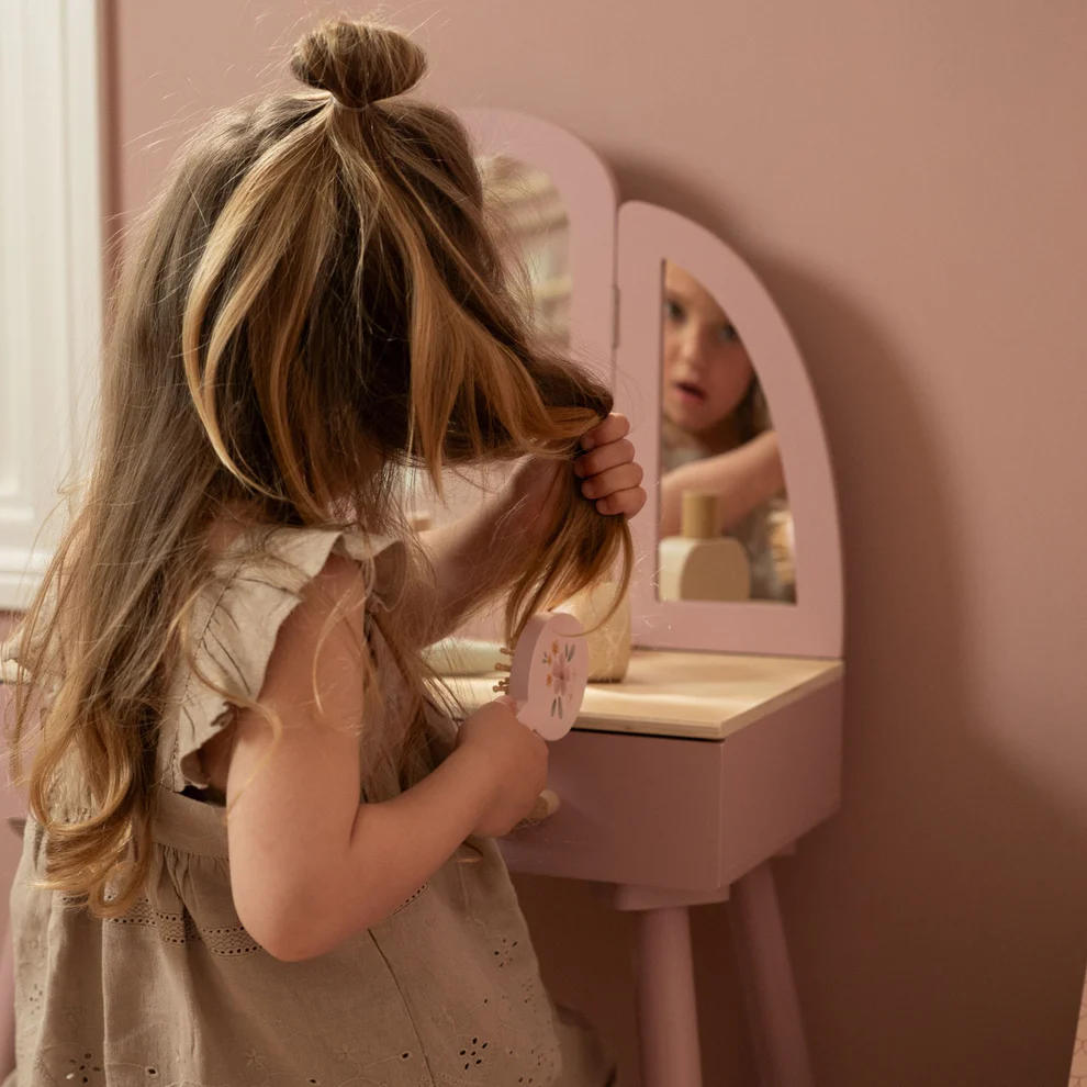 Menina penteando cabelo sentada junto a mesa de maquilhagem rosa com espelho.