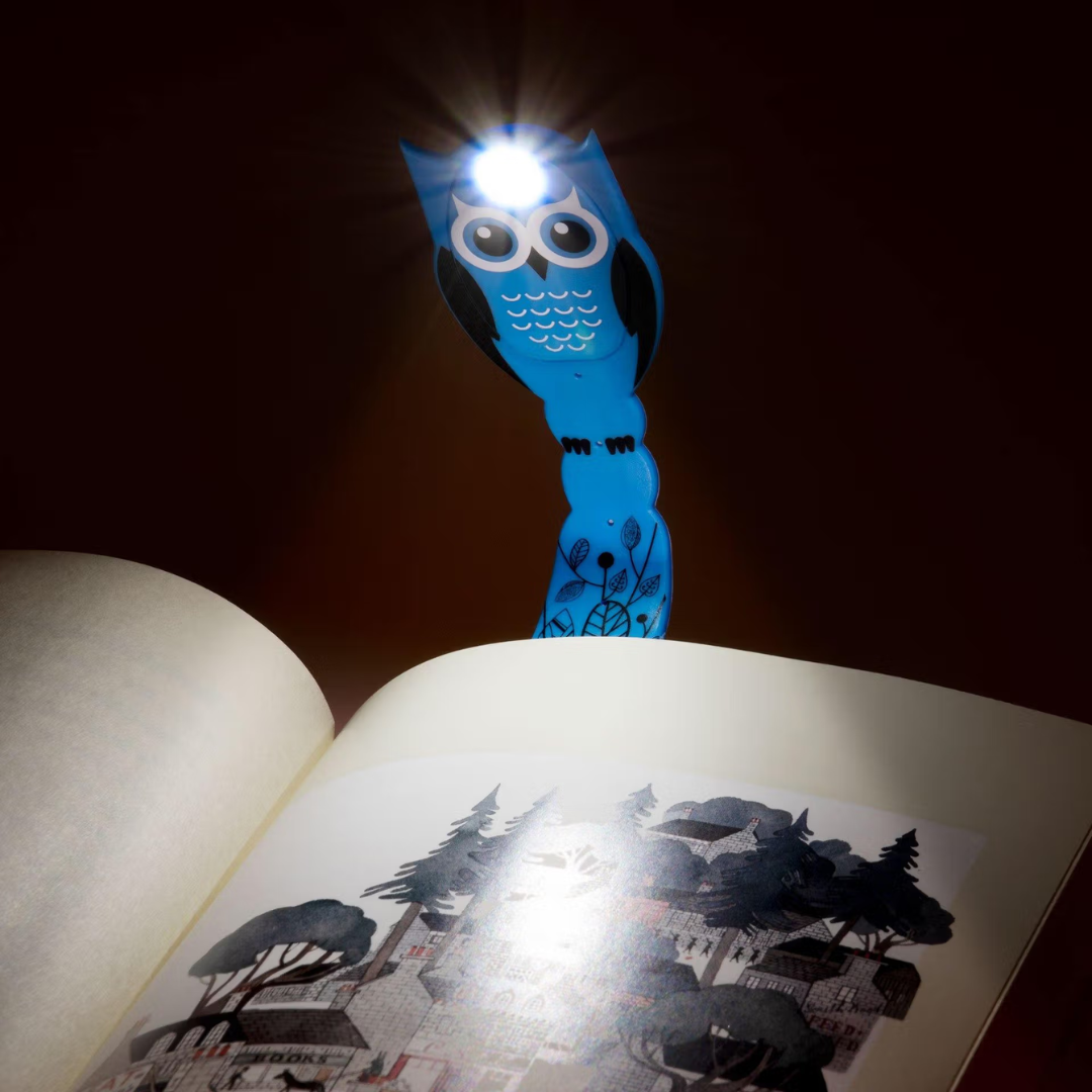 Luz de leitura azul em forma de coruja iluminando livro aberto com ilustração em preto e branco