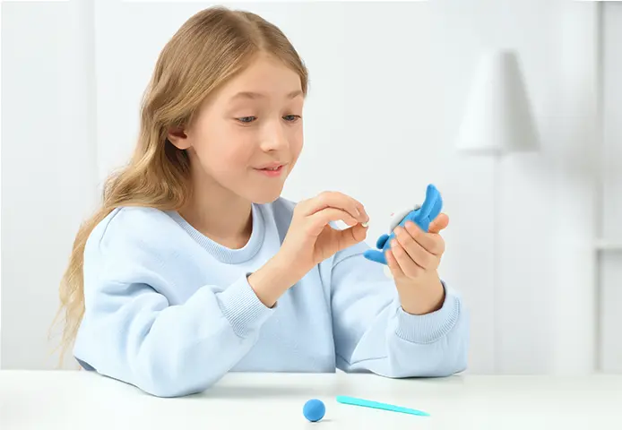 Menina loira com camisola azul clara segura dispositivo odontológico azul numa mesa branca