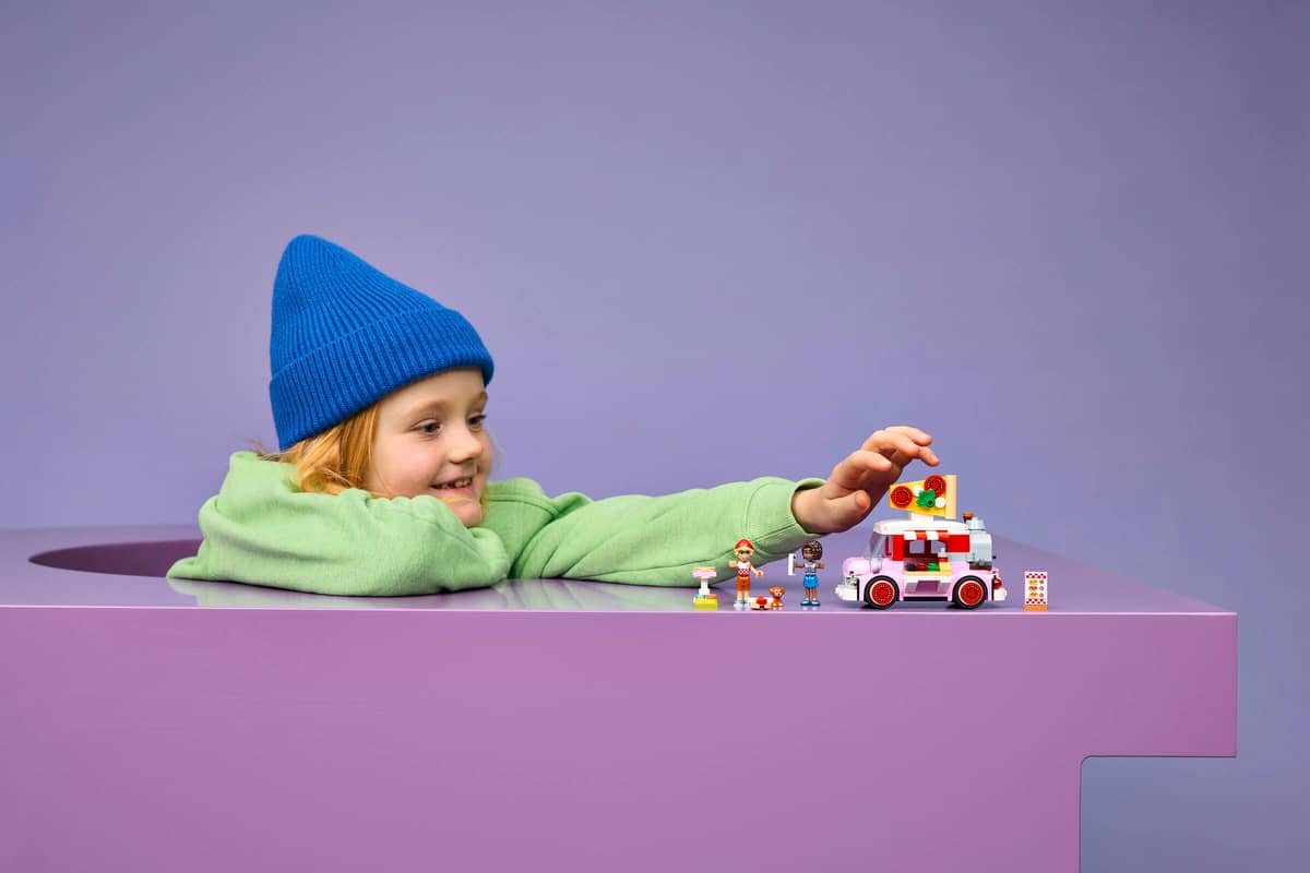 Criança a brincar com brinquedos Lego de carrinha de gelados e figuras sobre mesa roxa