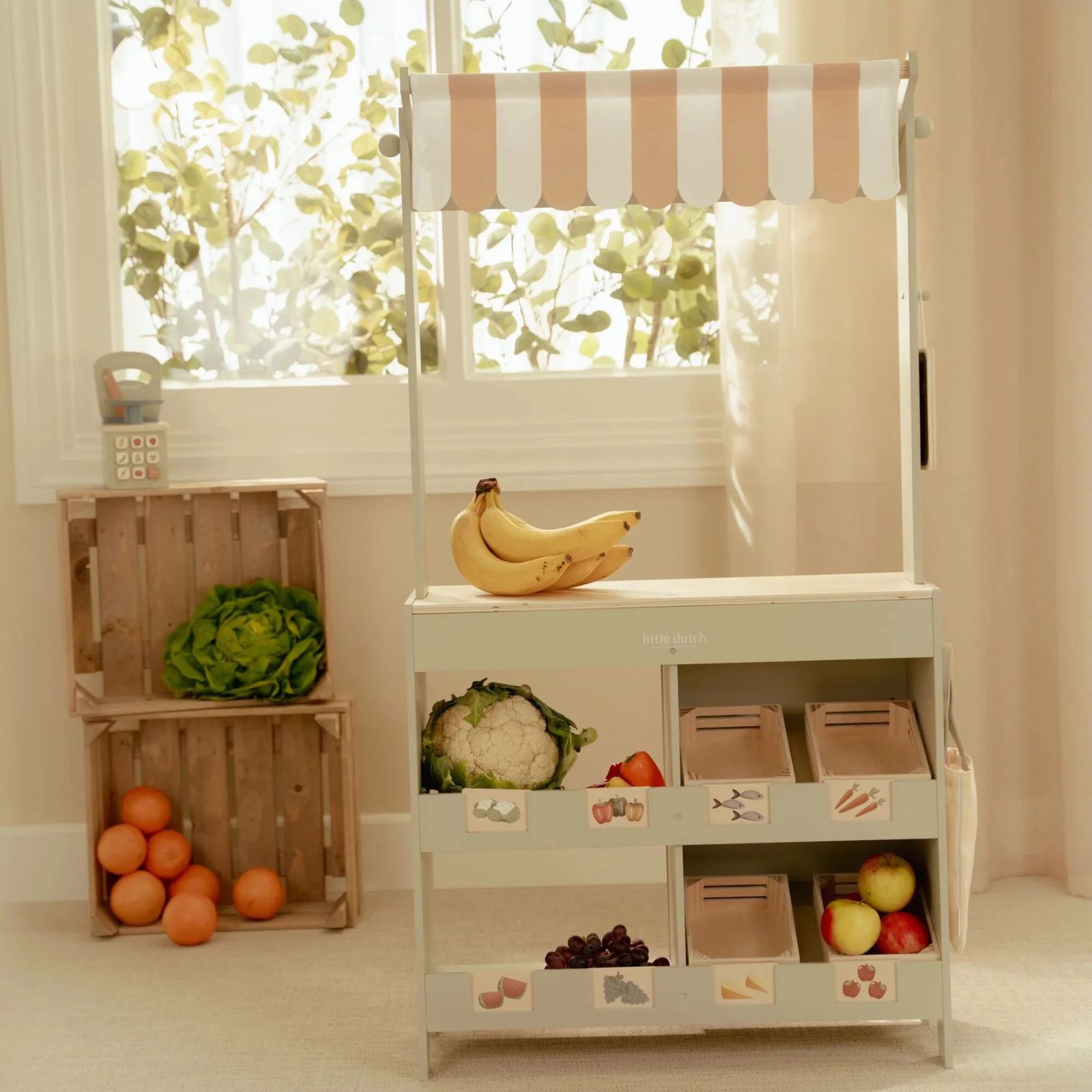 Carrinho infantil de madeira com frutas e vegetais, e caixas de madeira ao fundo com alface e laranjas
