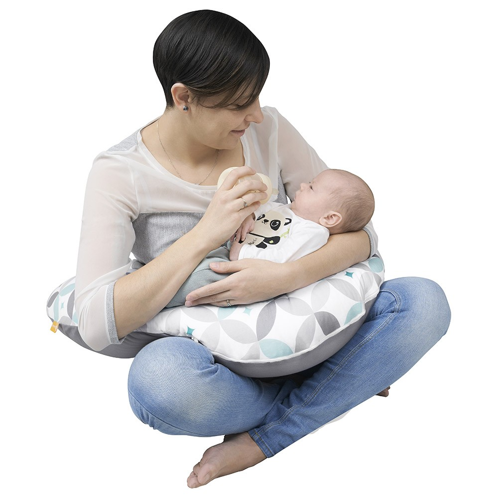 Mulher a usar almofada de amamentação cinzenta com padrão geométrico a amamentar bebé com body branco com panda.