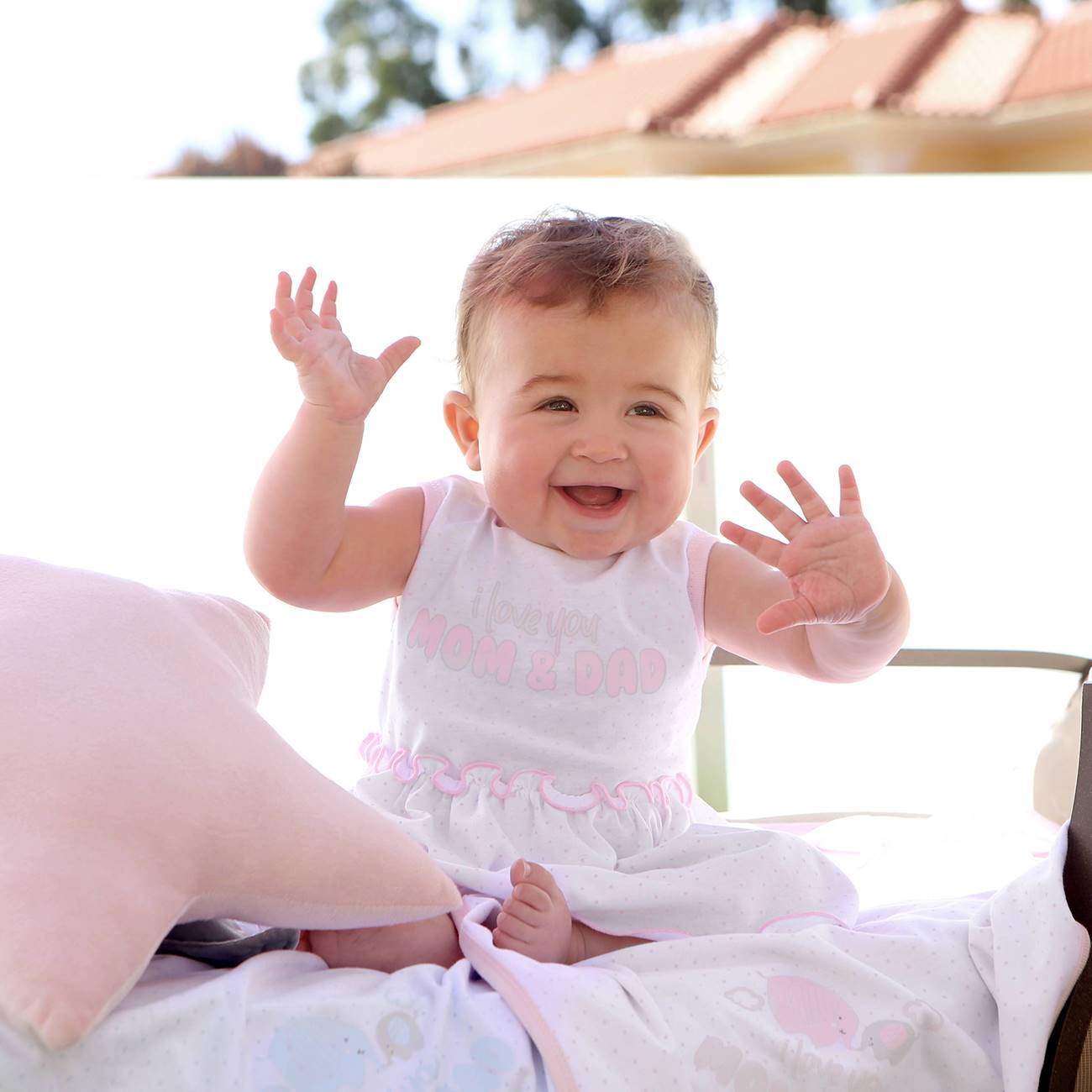 Bebé vestido de branco sentado em cama com manta e almofada cor de rosa ao ar livre