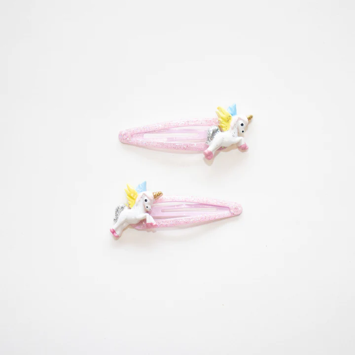 Ganchos de cabelo cor-de-rosa com figuras de unicórnios coloridos sobre fundo branco