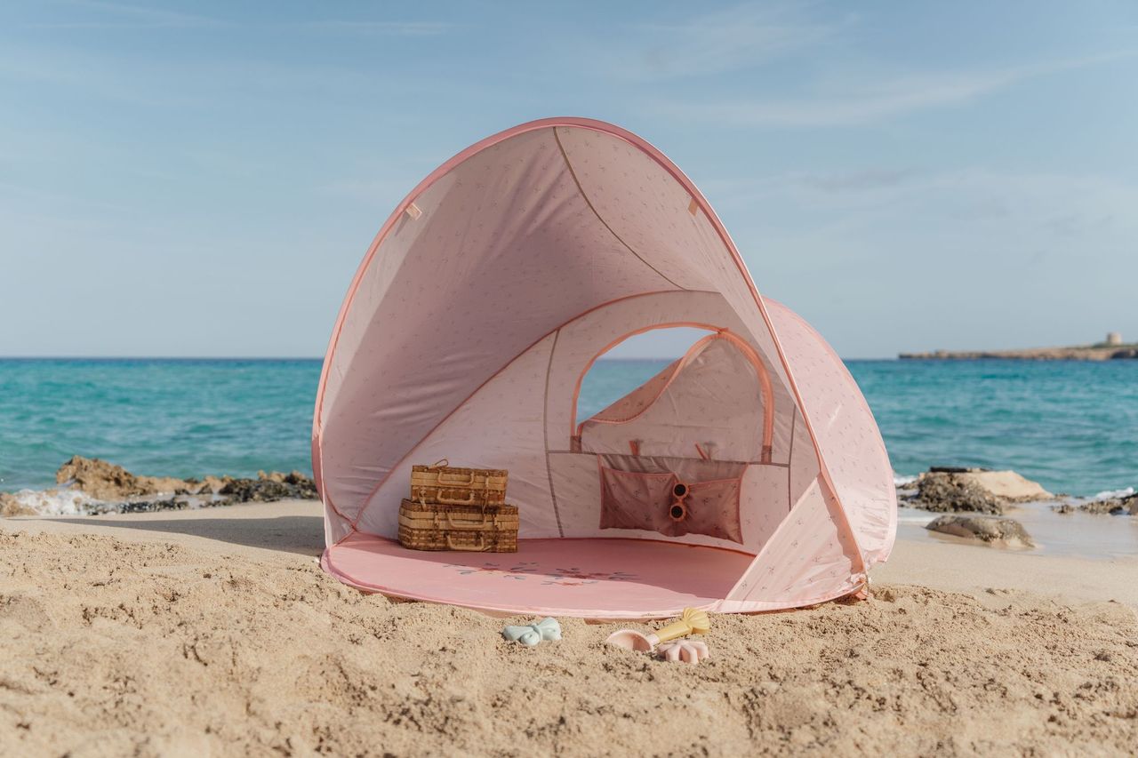 Tenda de praia rosa aberta na areia com mar ao fundo