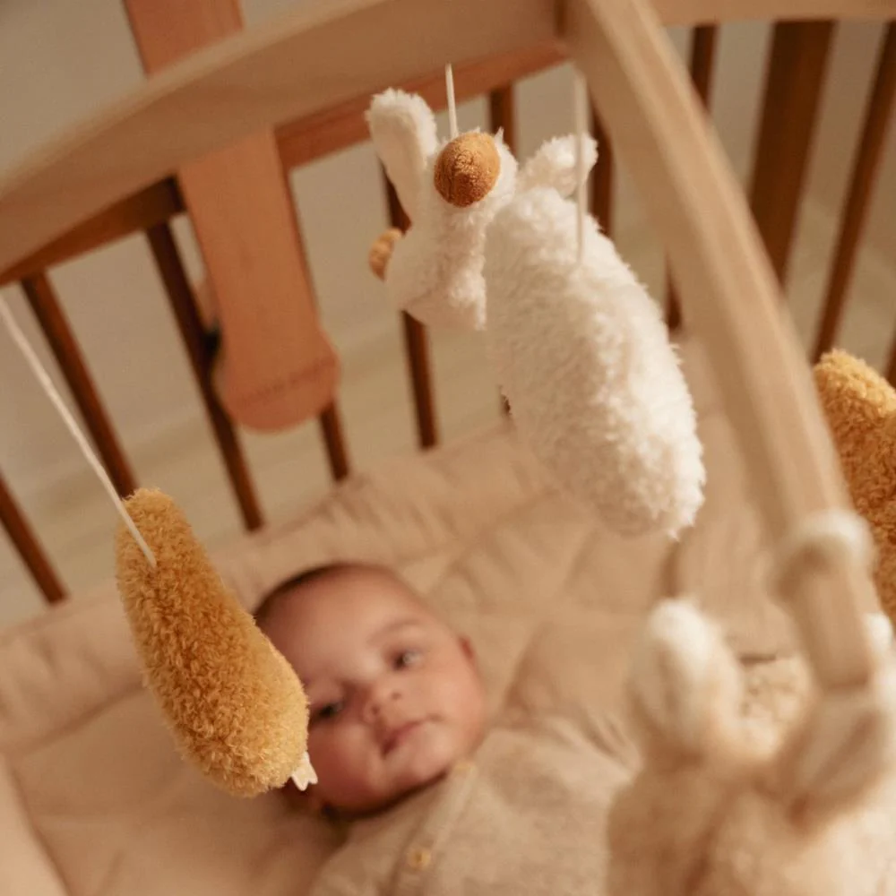 Móbile de berço em madeira clara com peluches e bebé deitado no berço.