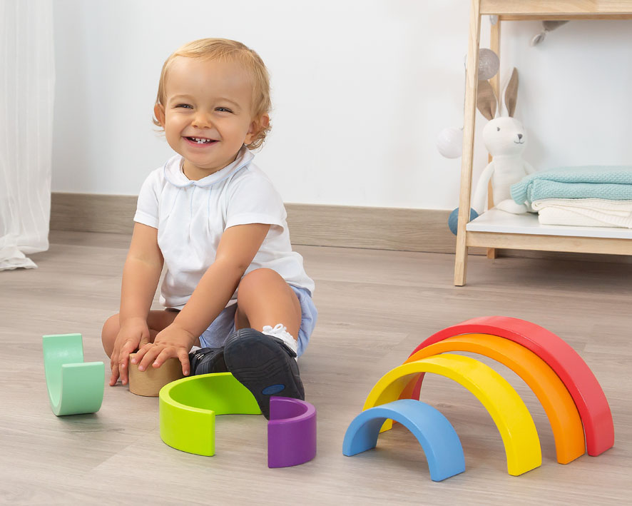 Criança sorridente brincando com blocos de arco-íris de madeira coloridos no chão de madeira clara