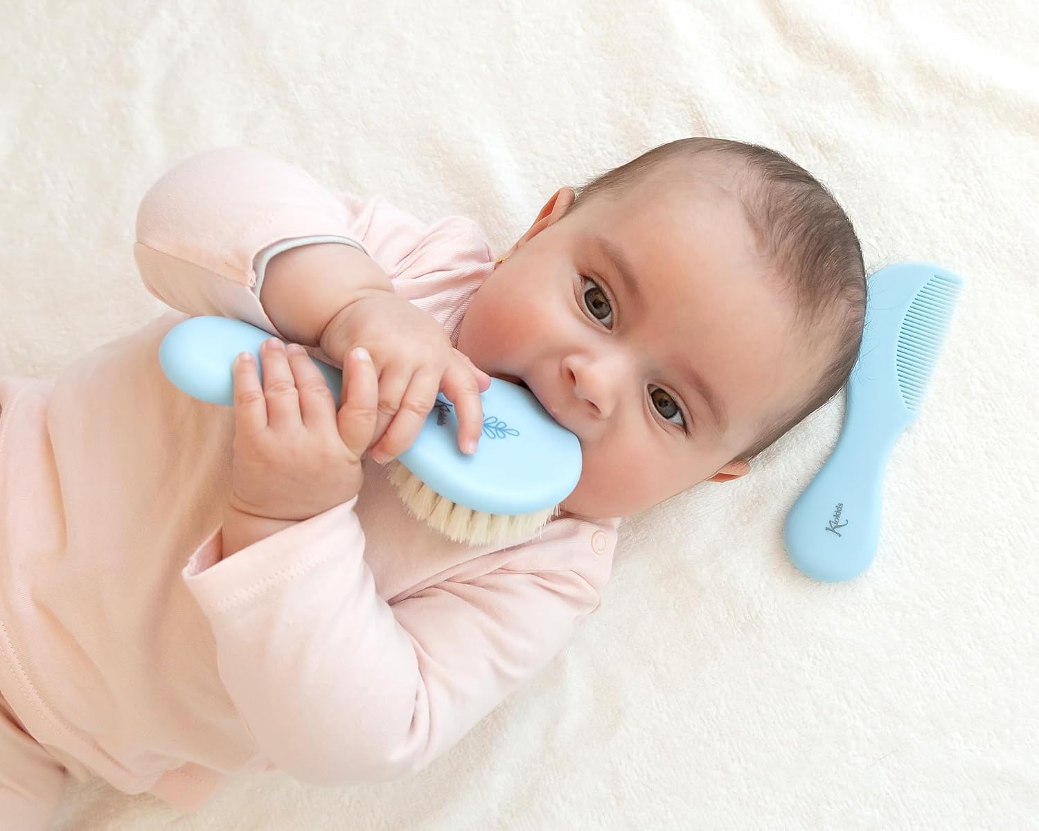 Bebé com escova azul e pente azul ao lado numa superfície branca