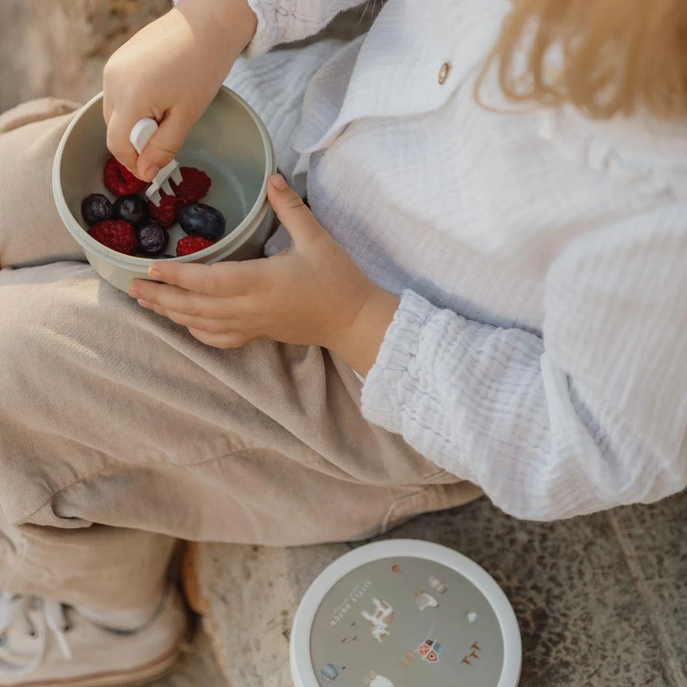 Criança com tigela cinza de frutos vermelhos e tampa decorada sentada
