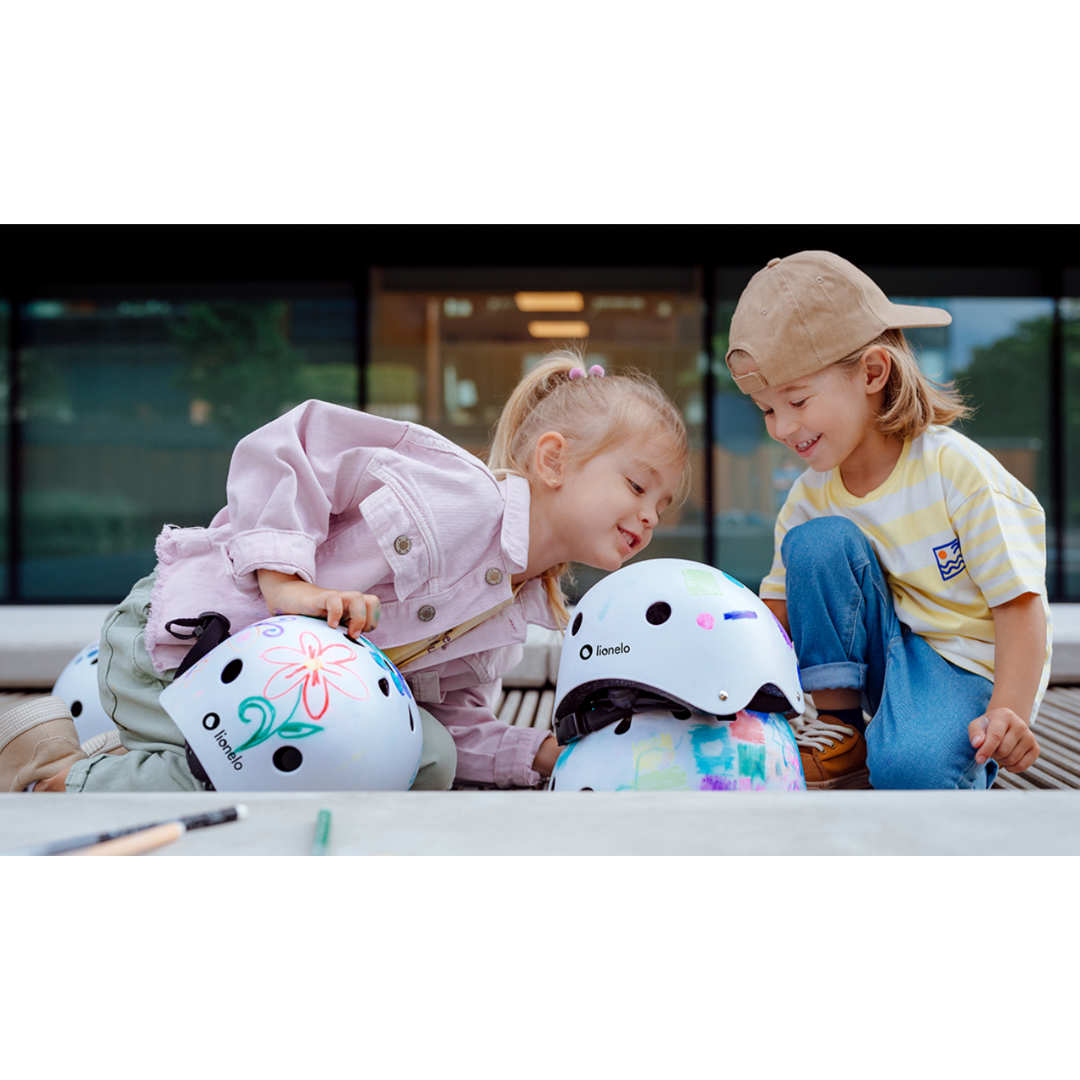 Duas crianças sentadas ao ar livre com capacetes decorados à sua frente